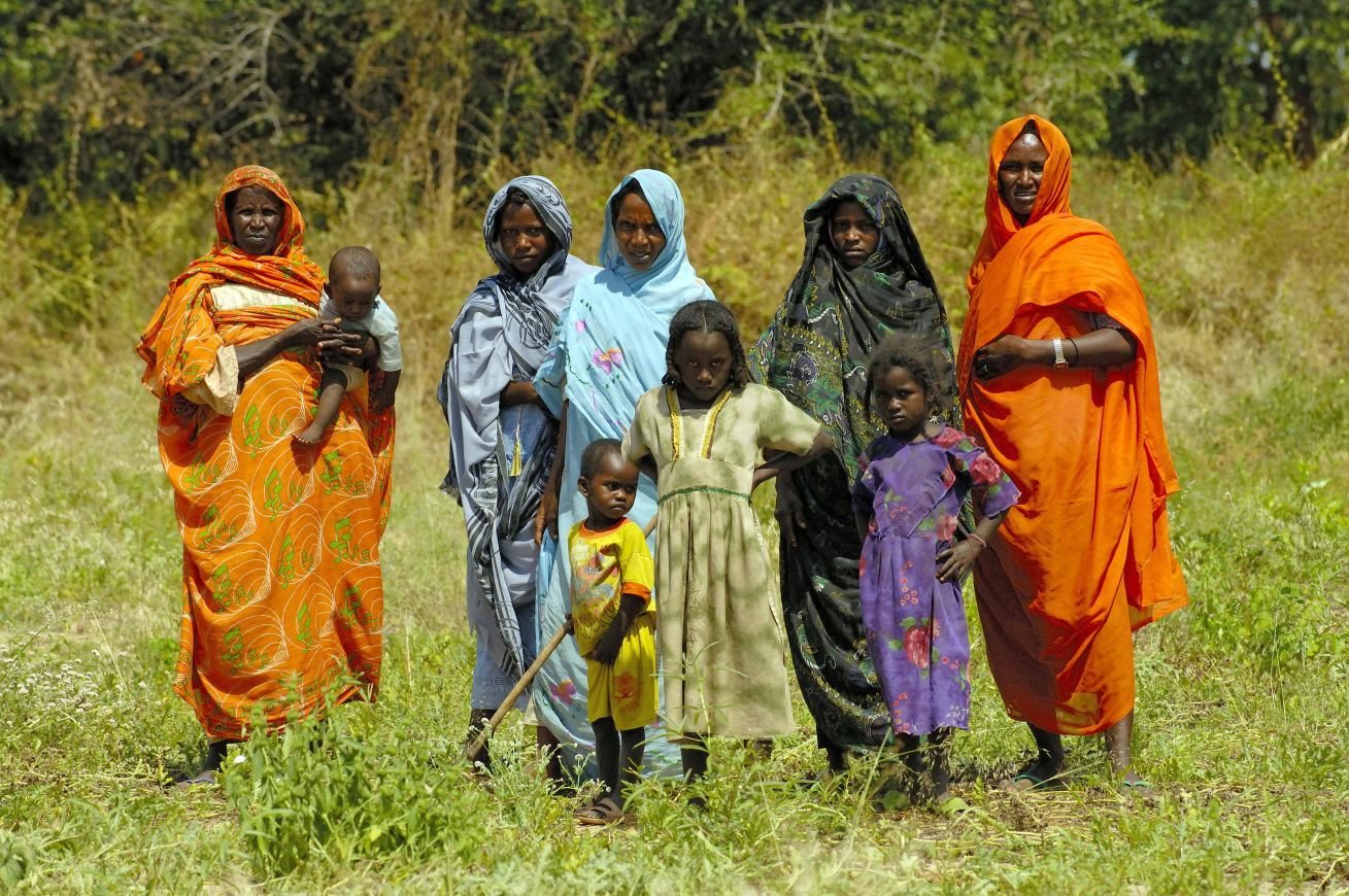 Women and children of an unreached tribe standing in a grassy field in bright traditional dress